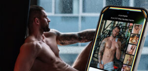Side profile of a tattooed, shirtless man resting by a rain-speckled window, with a large smartphone showing a dating app gallery beside him.