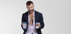 Man in a dark blazer shows two smartphones displaying apps to the camera.